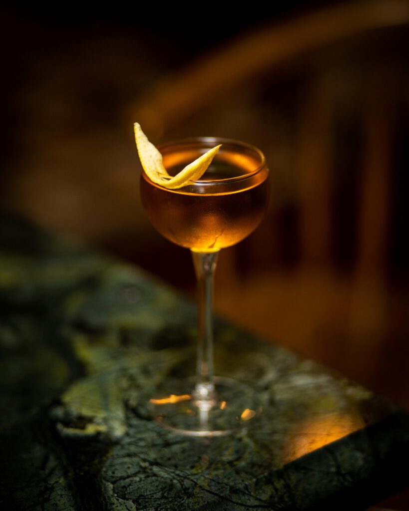 Coupe de champagne garnie d’un zeste d’orange, posée sur un comptoir de marbre vert dans une lumière tamisée